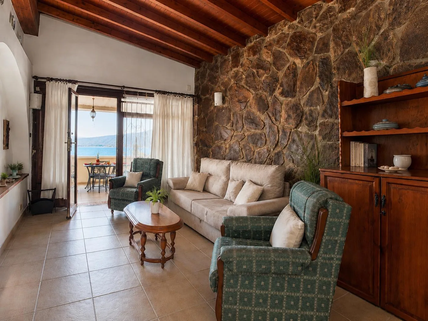 Salón de Casa Mariana con pared de piedra natural y el mar al fondo